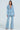 Against a light blue backdrop, a person with long brown hair wears the DIAMONDS DANCING DENIM BLAZER—a light blue sequined oversized longline silhouette with flared pants. They complete their look with open-toed heels.