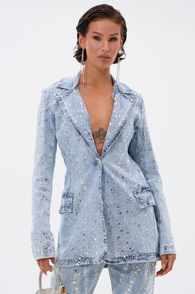 A woman models the DIAMONDS DANCING DENIM BLAZER in light blue with matching pants, accessorized with large hoop earrings and a metallic handbag, standing confidently against a plain white background.