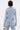 A person with short, wet-look hair is seen from the back wearing the DIAMONDS DANCING DENIM BLAZER, adorned with sparkling silver sequins. They hold a small metallic handbag, highlighting this dazzling statement piece.