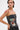 A person with hoop earrings and face piercings wears the ARTS AND CRAFTS PATCH WORK DENIM CORSET, featuring lace-up panels and colorful patches, with a red painted shoulder design, posing against a plain background.