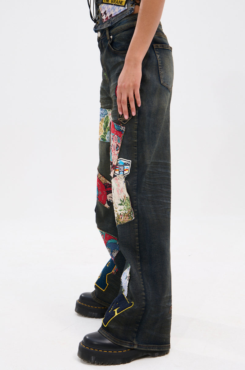 Someone models the ARTS AND CRAFTS PATCH WORK DENIM PANTS, featuring colorful designs and a high-waisted fit, paired with black platform shoes against a plain white background.