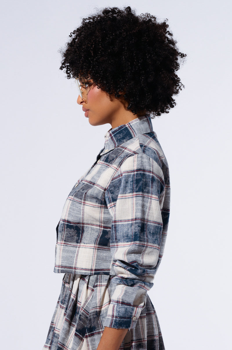 A person with curly hair and glasses is stylishly dressed in a Bella Plaid Pleated Mini Skirt and a classic Bella Plaid Button Down Shirt, made from 100% cotton. The individual is shown in profile against a plain background. 1