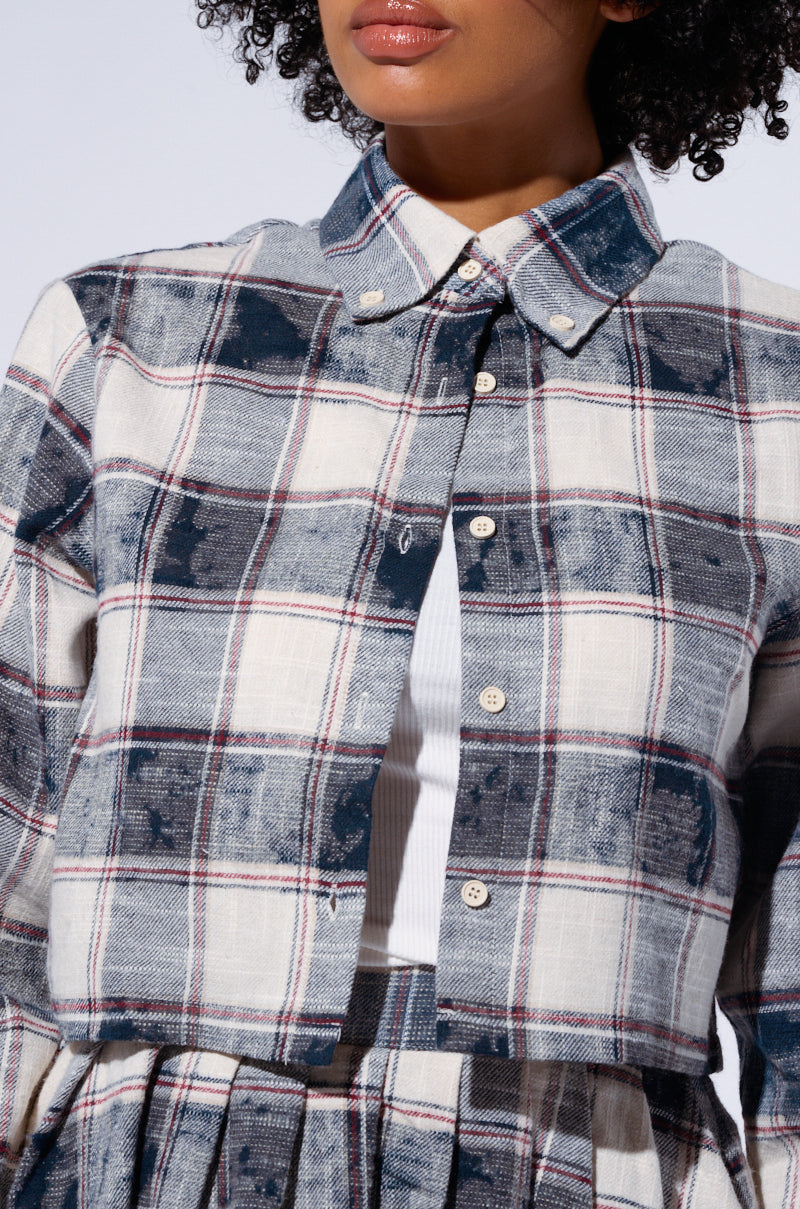 Close-up of a person wearing the BELLA PLAID BUTTON DOWN SHIRT in white, blue, and red over a white top. The shirt's textured pattern complements the Bella Plaid Pleated Mini Skirt. The person's curly hair is visible, but their face remains partially hidden. 5
