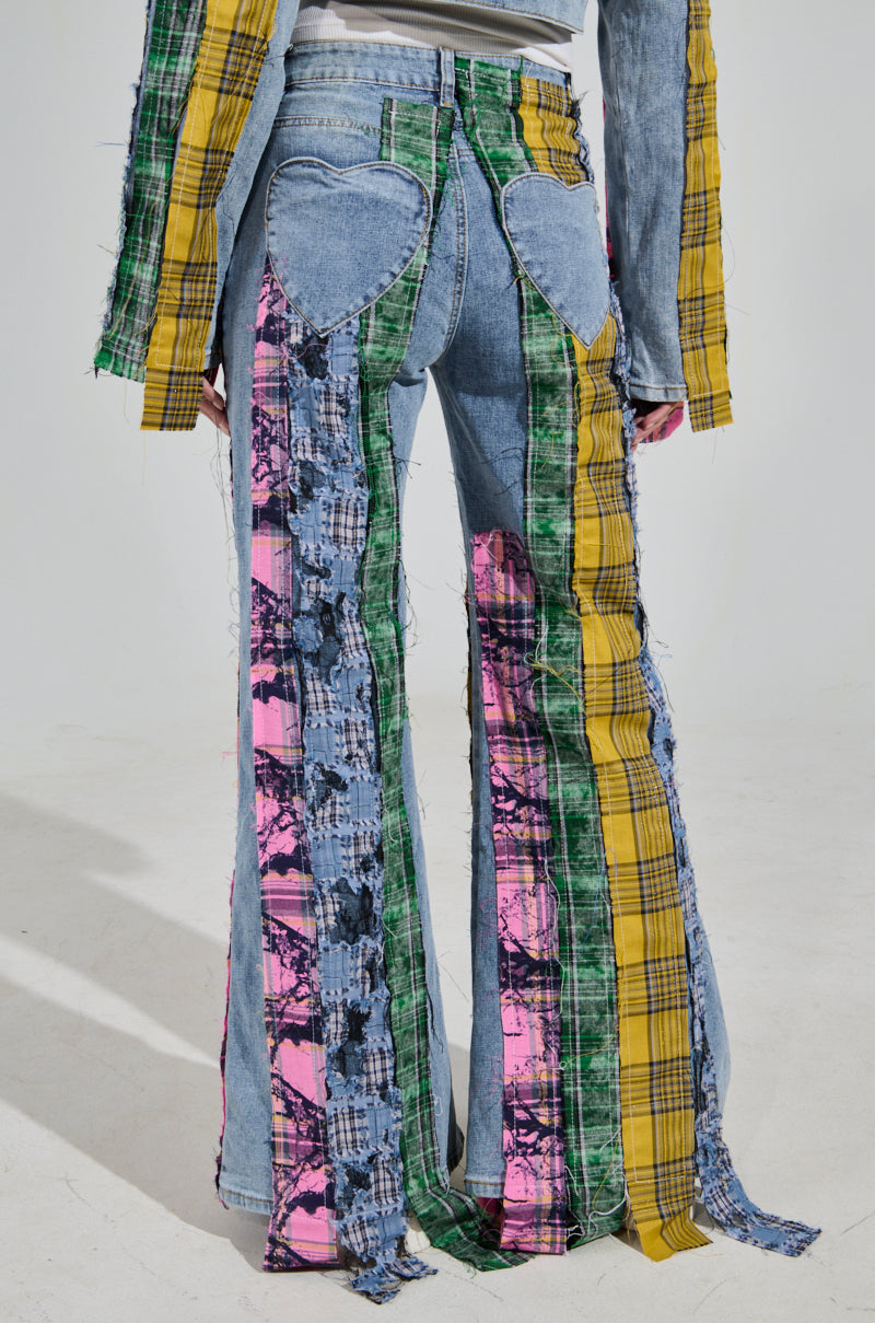 The MAKING WAVES PATCHWORK FLARE DENIM showcases a back view with colorful plaid and tie-dye designs. High-rise fit features heart-shaped pockets and matching long sleeves. Distressed plaid flannel patches in yellow, green, pink, and blue adorn the light denim base.