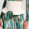 A person wearing a vibrant, multicolored, long-sleeve dress with an abstract, wavy pattern. The dress features a high slit on one side and is cinched at the waist by the ULTIMATE FEMME PEPLUM PU BELT, which is structured and off-white with peplum detailing. The person's head is not visible.