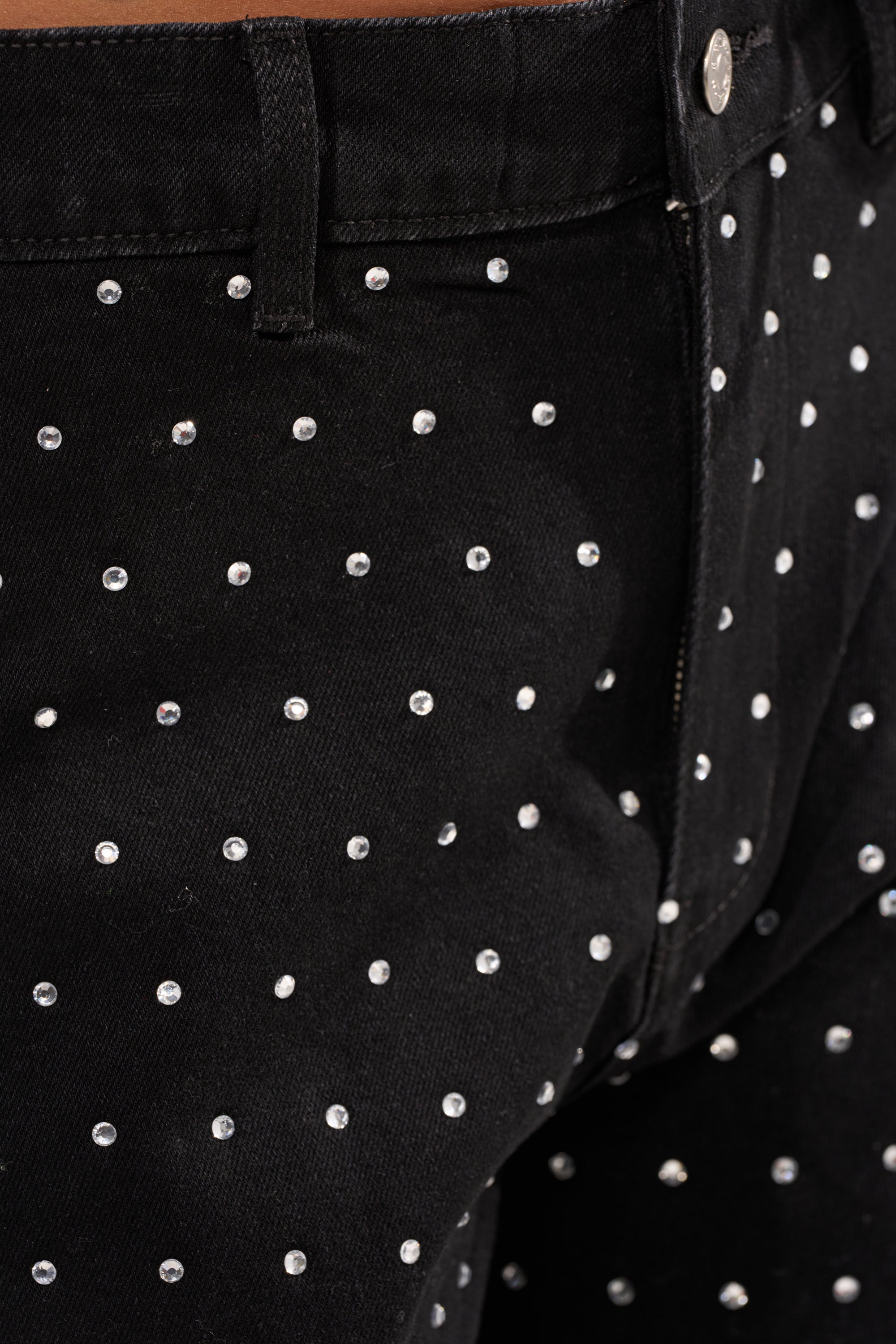 Close-up of the ITS GIVING BERMUDA SHORT featuring black rhinestone denim, evenly spaced small silver studs, a high-rise waist, waistband, belt loop, button, and upper thigh area. 7
