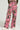 A person faces away from the camera, wearing the STAND OUT TO FIT IN CARGO PANTS, which feature a pink and black abstract pattern with a high-rise fit. These wide-legged cargo pants come with side pockets and are paired perfectly with white sneakers.