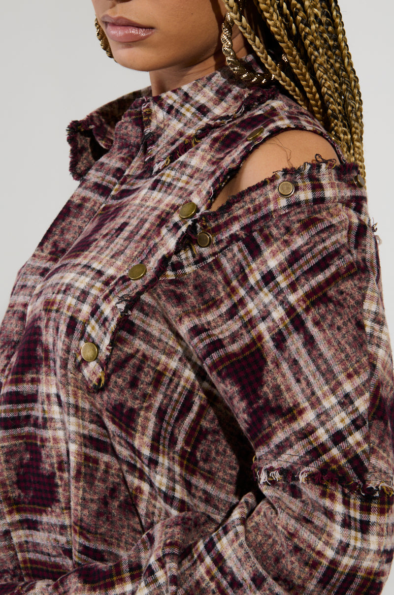 A close-up shows someone wearing the DRIFTER FLANNEL, which boasts a unique design with distressed detailing, button accents, and a cut-out shoulder. Their braided hairstyle is paired perfectly with gold earrings. The grunge flannel pattern artfully blends shades of maroon, beige, and black.