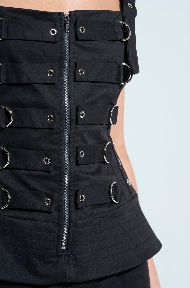 A close-up of the AMELIA JUMPSUIT WITH METAL DETAILS shows a black corset featuring a front zipper, intricate metal elements like buckles and D-rings, detailed stitching, and a structured design against a light background.