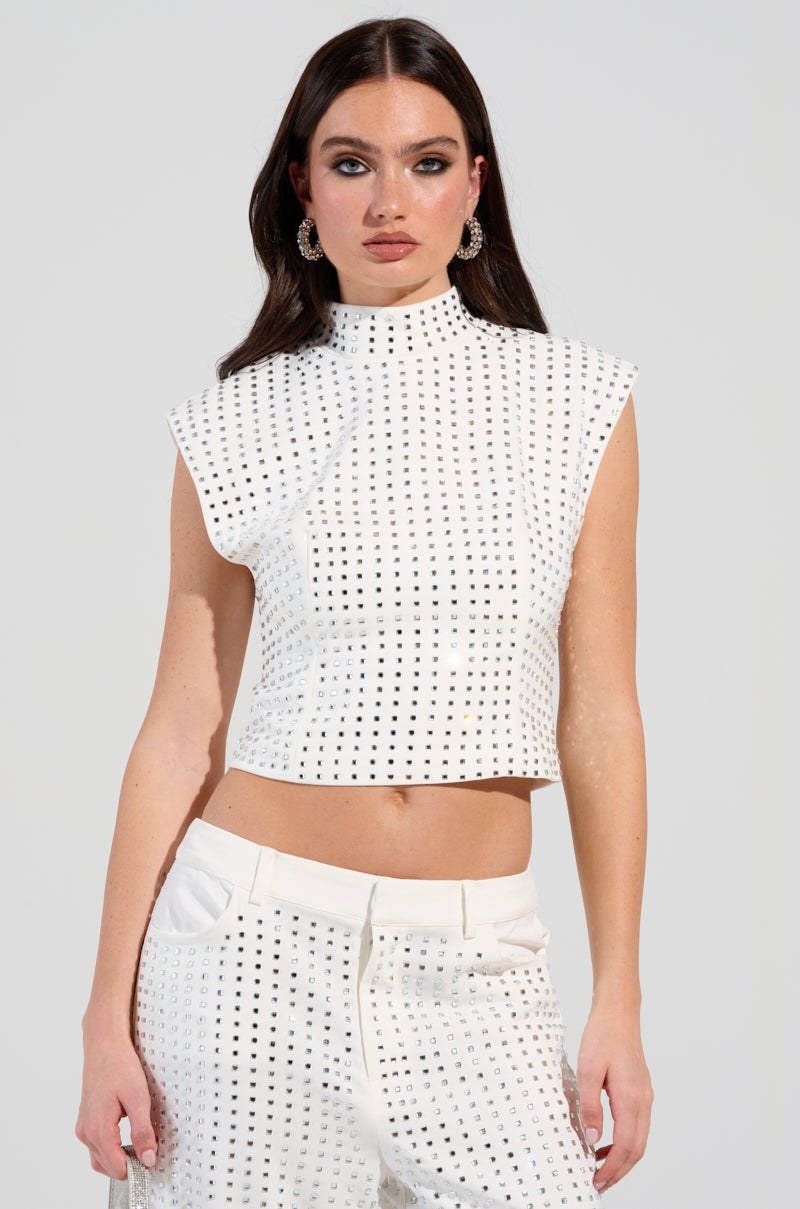 A woman models an ICED OUT TOP, showcasing a white, short-sleeved design paired with coordinating pants that feature a dotted pattern. Her long dark hair flows elegantly, accentuated by hoop earrings, while the simple light background provides a striking contrast to her ensemble.