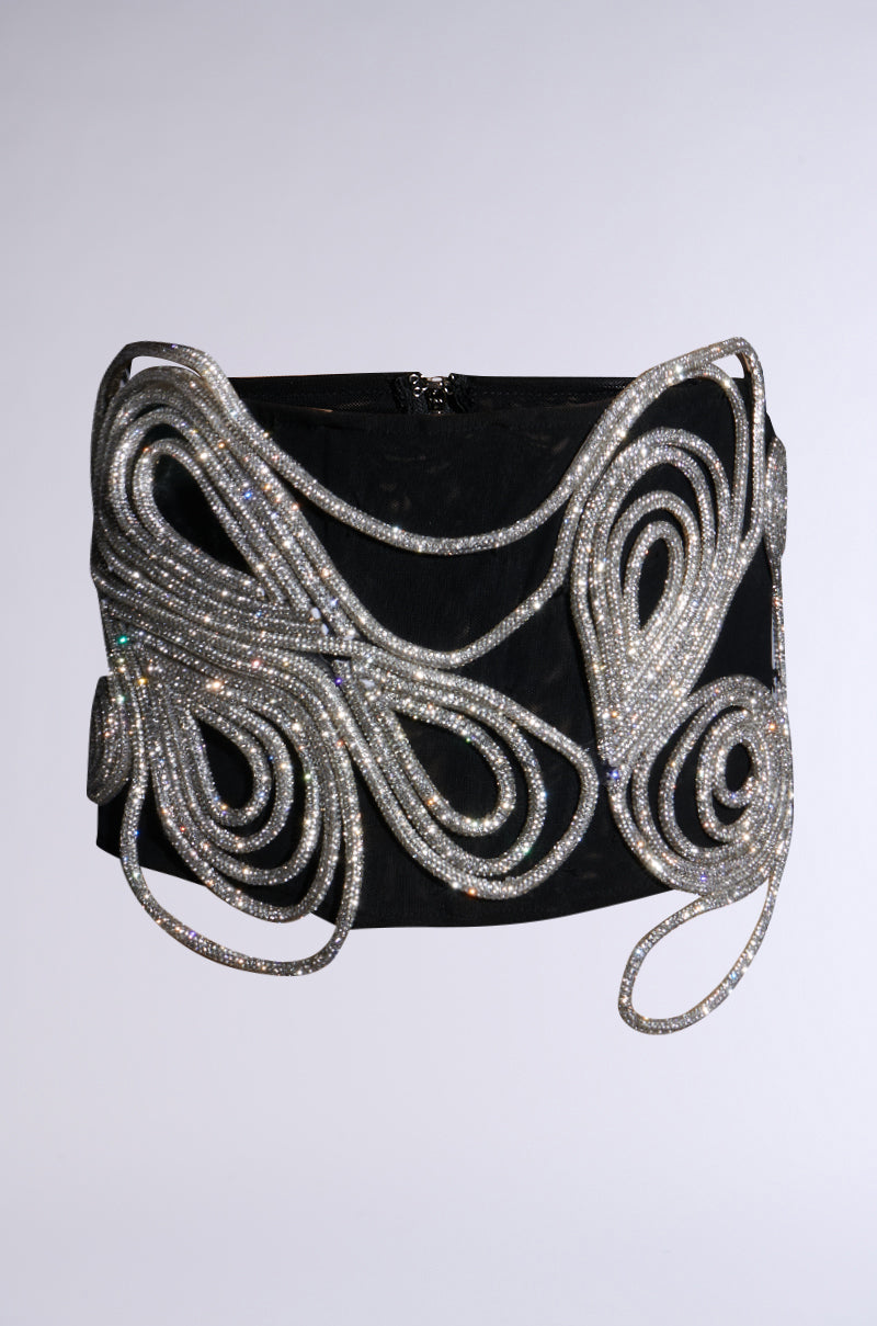 The IM A WONDER RHINESTONE STRETCH BELT boasts intricate, looping silver embellishments, reminiscent of a rhinestone belt, elegantly draped across its black surface. The sparkling silver details provide a striking contrast against the dark backdrop.