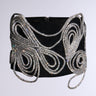 The IM A WONDER RHINESTONE STRETCH BELT boasts intricate, looping silver embellishments, reminiscent of a rhinestone belt, elegantly draped across its black surface. The sparkling silver details provide a striking contrast against the dark backdrop.