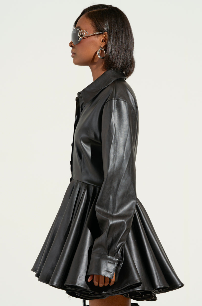 A person in profile against a light background is adorned with short hair, large hoop earrings, and sunglasses, elegantly showcasing the modern chic style of THE IT GIRL MINI DRESS IN BLACK PU by AKIRA Label. The faux leather dress highlights a flared skirt and long sleeves.