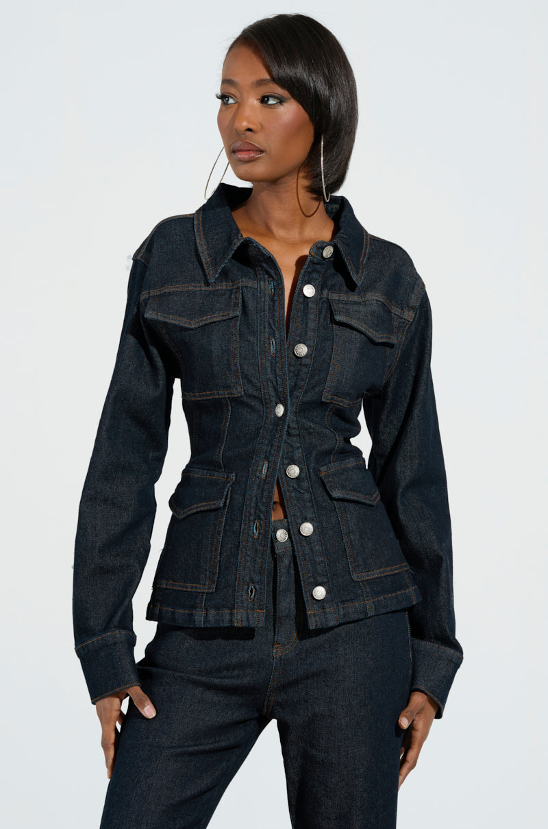 A person sporting an EVERYDAY LIVIN' DENIM BUTTON DOWN SHIRT and matching dark wash jeans poses against a plain background. The shirt, ideal for daily wear, includes chest and side pockets, enhancing their long hair for a chic and effortless style.