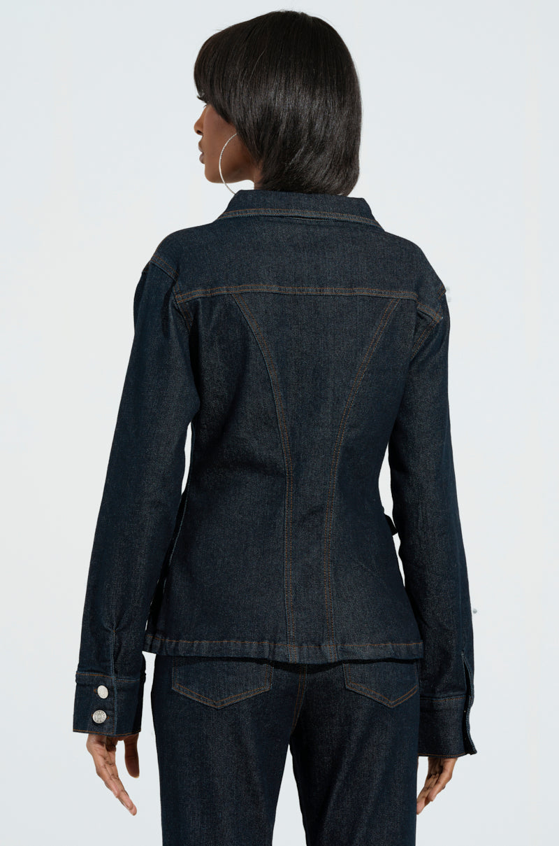 With their long hair flowing, a person stands with their back turned, embodying the everyday livin' vibe in the EVERYDAY LIVIN' DENIM BUTTON DOWN SHIRT paired with matching jeans. The shirt showcases prominent seams and buttoned cuffs, reminiscent of a classic denim design, while the jeans feature a dark wash denim look with noticeable back pockets against a light background.