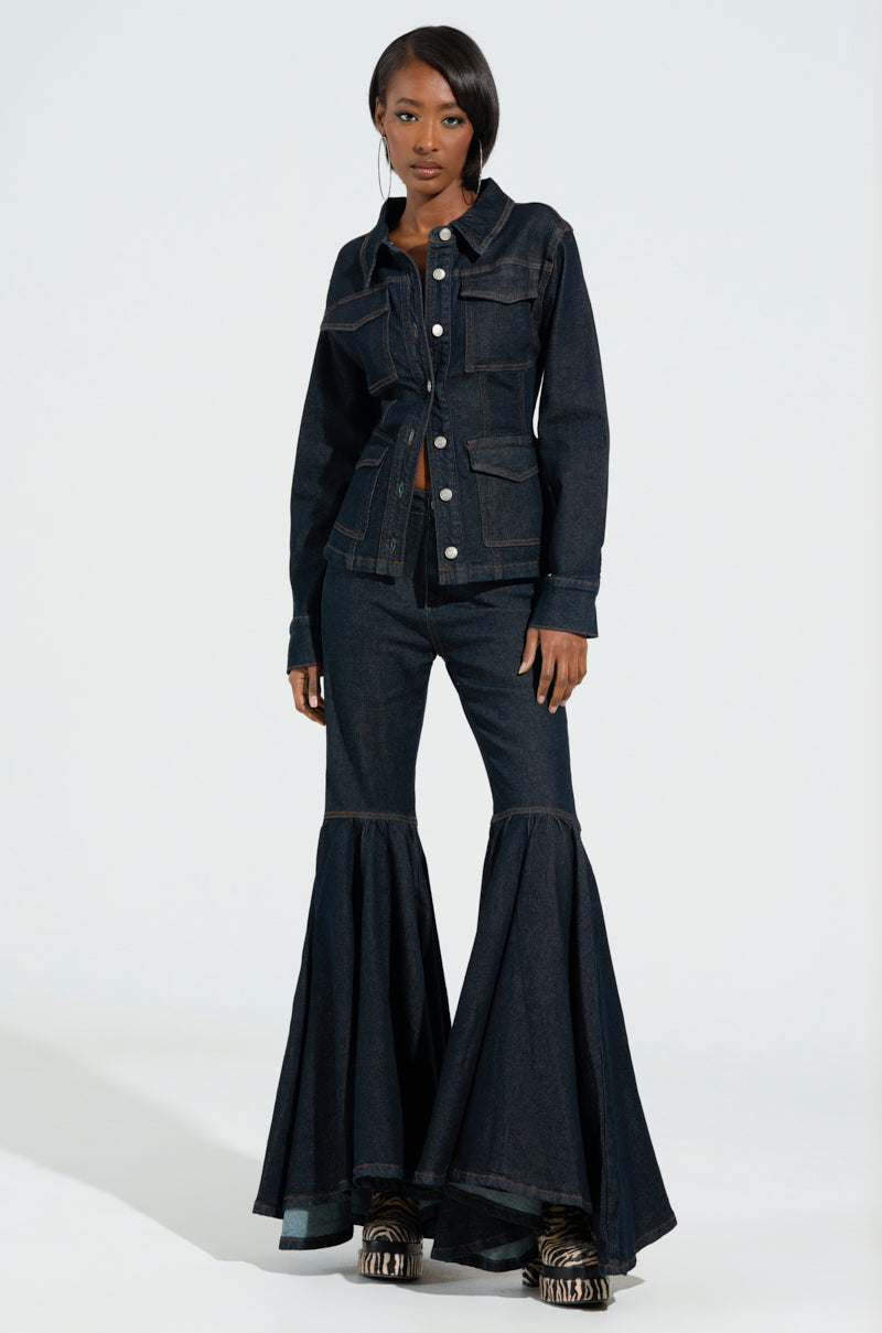 A person sporting the EVERYDAY LIVIN' DENIM BUTTON DOWN SHIRT, paired with dark wash flared pants accentuated by large pockets and button details. They stand in a relaxed pose against a plain, light background, their hands resting by their sides, embodying the perfect blend of style and comfort.