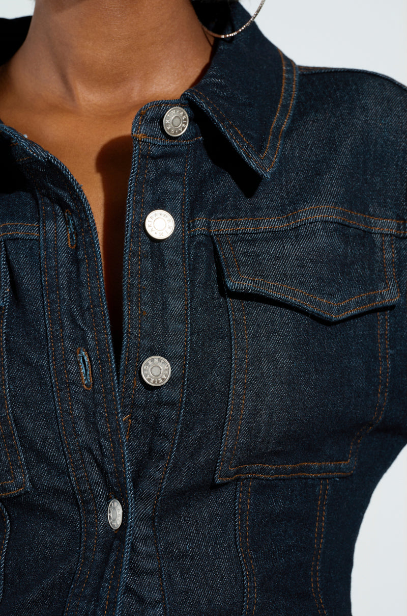 A close-up of someone wearing the EVERYDAY LIVIN' DENIM BUTTON DOWN SHIRT showcases its dark wash denim, visible orange stitching, and silver buttons. This versatile piece includes two chest pockets and is partially unbuttoned to reveal the collar and upper chest area.