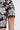 A close-up of someone wearing the FLORAL SEQUIN MESH SHORT SLEEVE BLOUSE, featuring black mesh fabric with prominent white floral embroidery and shimmering silver sequin details.