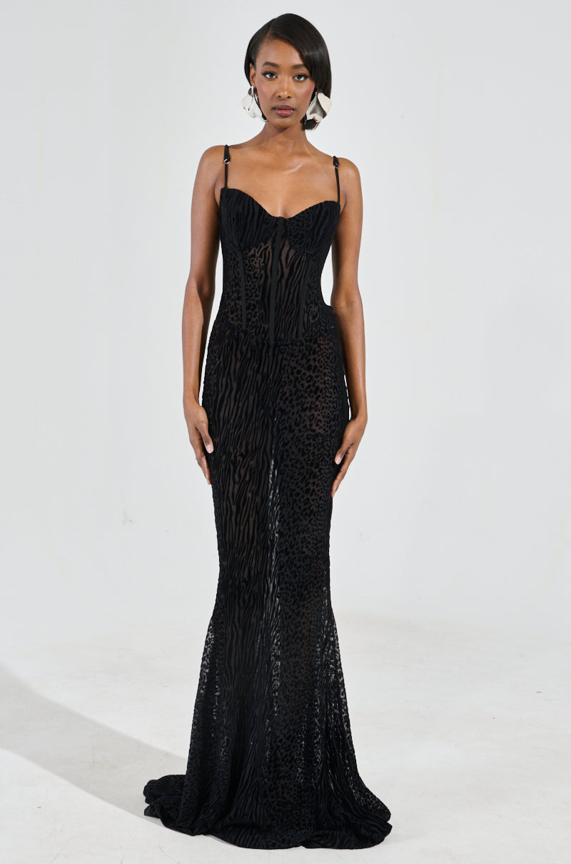 Someone is wearing the ON YOUR FYP PRINTED VELVET BURNOUT MAXI DRESS, which is a long and sleeveless gown featuring a subtle animal print design. The sheer mesh fabrication enhances its elegance, as the fitted bodice gracefully extends to the floor. This sophisticated outfit stands out against a plain white background.