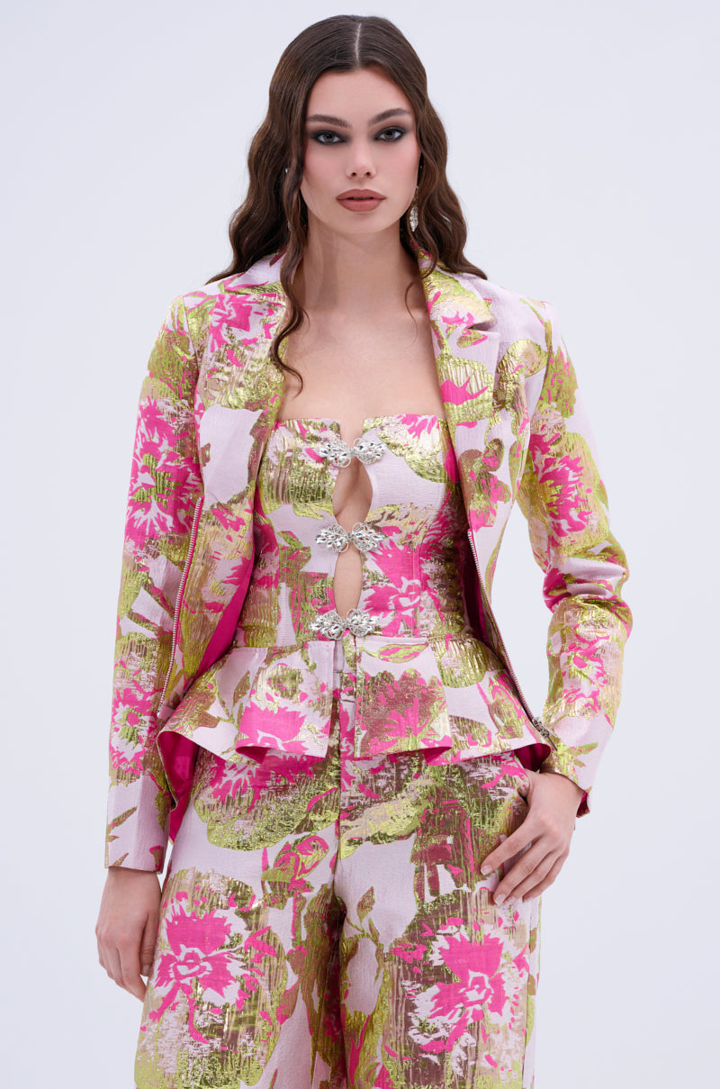 A woman wears the LOVELY FLORAL BROCADE BLOUSE—a stylish pink, gold, and green floral top with cut-out details and jeweled embellishments—paired with matching pants, standing against a plain light background.
