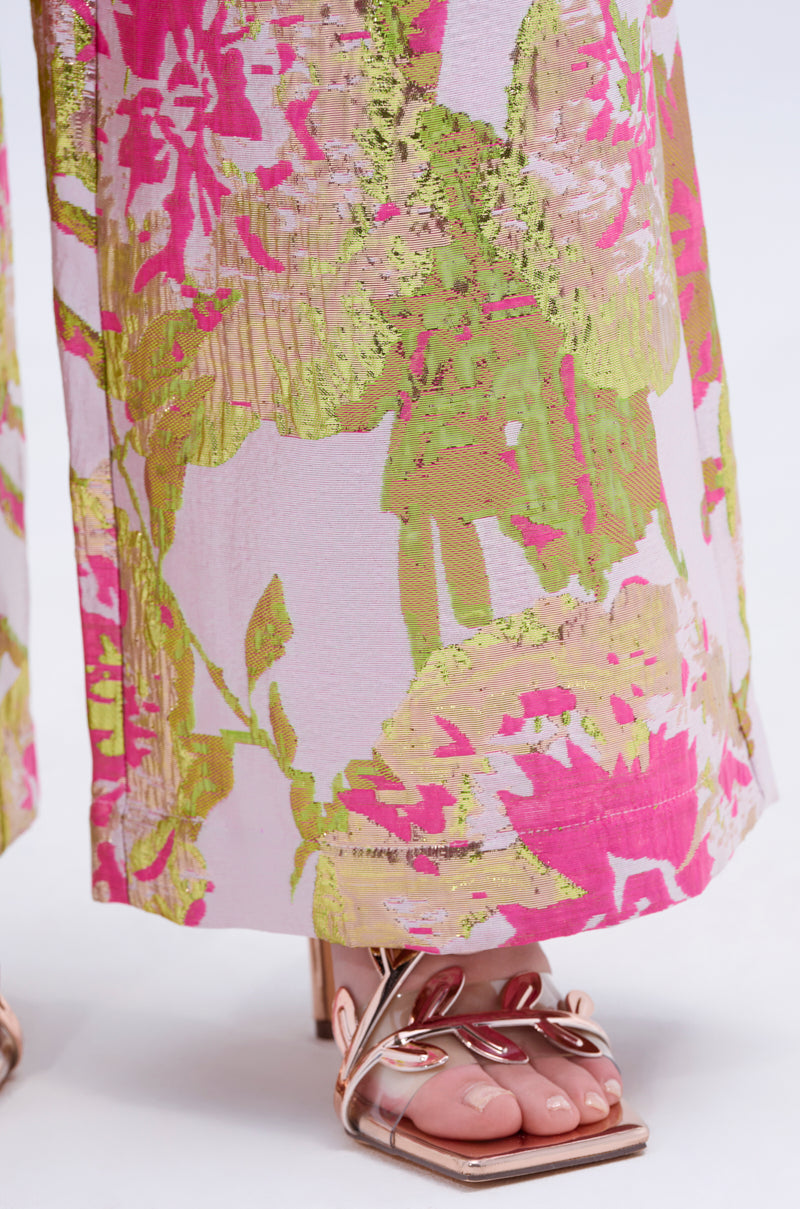 A close-up of a person wearing the LOVELY FLORAL BROCADE TROUSER, wide-leg with pink, green, and gold metallic floral details, styled with open-toe rose gold heels.
