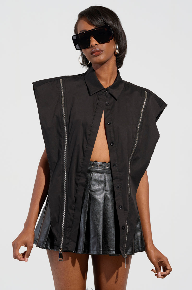 A person wearing the edgy-chic BAD GIRL ZIPPER DETAIL BUTTON DOWN SHIRT complements it flawlessly with a black leather skirt. They also sport oversized black sunglasses and hoop earrings against a plain, well-lit background that enhances their bold style statement.