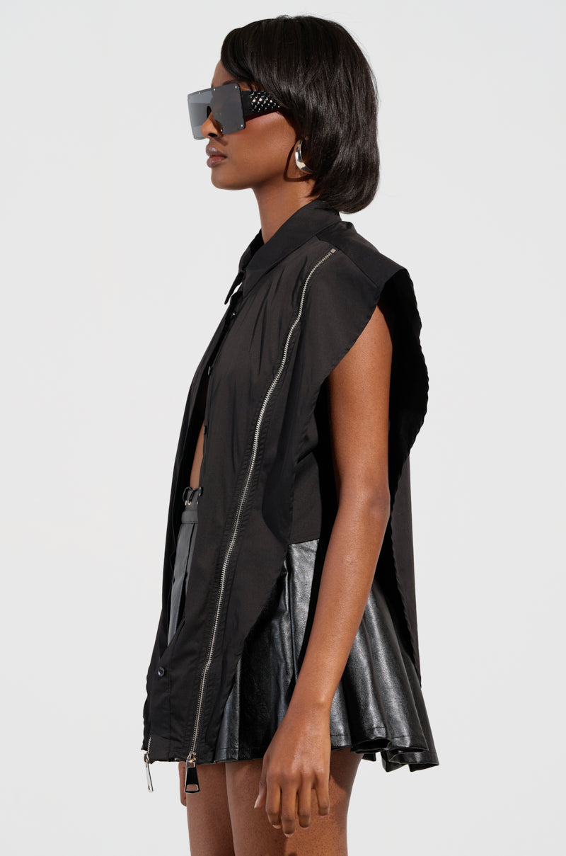 A person in profile is wearing the BAD GIRL ZIPPER DETAIL BUTTON DOWN SHIRT with metallic zipper accents, paired with matching black leather shorts. Their short hair pairs flawlessly with the oversized sunglasses and hoop earrings. The plain white background emphasizes the outfit's bold statement.