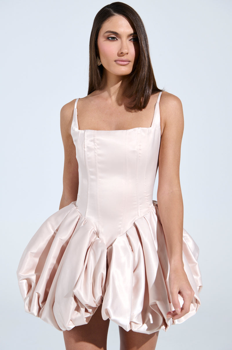 A woman wears the JULIET SATIN MINI DRESS IN LIGHT PINK, which features a strapless design with a voluminous bubble skirt. Her long, straight hair flows down as she poses against a soft background.
