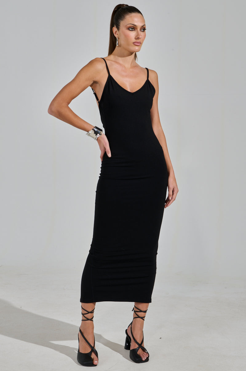 The woman exudes elegance in a MY GOODIES SEAMLESS MAXI DRESS, showcasing its sleeveless bodycon silhouette paired with strappy heels. Her ponytail adds flair, and bracelets add a chic touch, while the stretchy material ensures comfort as she poses effortlessly against the plain backdrop.
