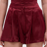 A person wearing the RED HOT FLOUNCY SHORT in a rich burgundy satin with a matching top; the image is cropped from midriff to thighs.