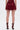 Facing away, a person wears the RED HOT FLOUNCY SHORT in rich burgundy satin with matching strappy high-heeled sandals featuring gold buckles, set against a plain white background.