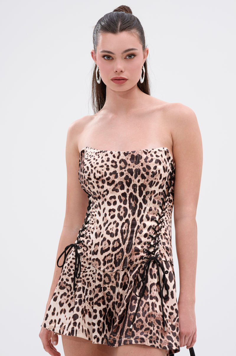 A woman with long dark hair in a high ponytail wears the LOVING YOU IS EASY CHEETAH CORSET, a strapless, fitted mini dress with cheetah corset details and lace-up panels. She pairs it with large hoop earrings and a small black bag. 0