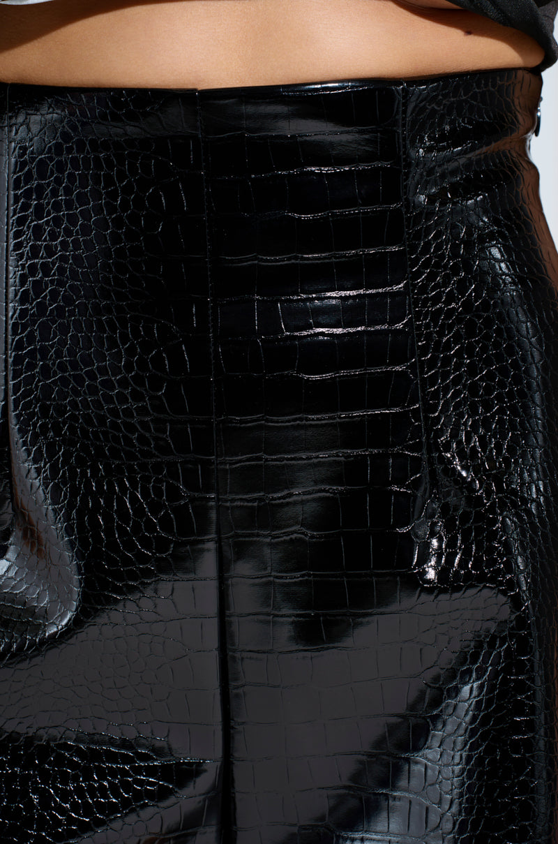 A close-up of a person wearing the MY LIFE CROC SHORT, a glossy, high-rise faux leather skirt with an embossed snakeskin pattern. The material reflects light for a sleek and textured look.