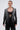 A woman with slicked-back hair models the MILA EMBELLISHED BLAZER IN BLACK with silver sequin stripes, a black lace bralette, matching stretch pants, dangling earrings, and a silver clutch against a plain backdrop.