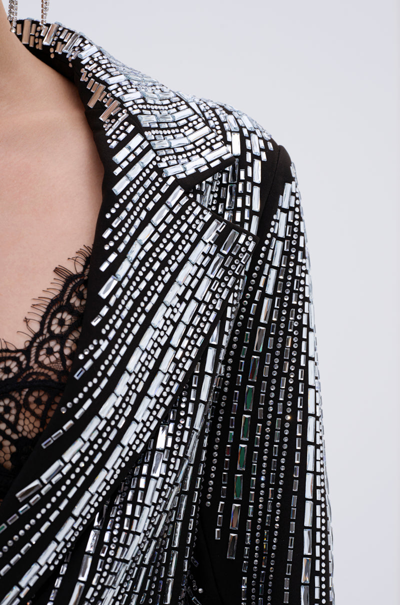 A close-up of a person wearing the MILA EMBELLISHED BLAZER IN BLACK, a sparkly blazer with rows of reflective silver rectangular beads over a black lace top for a bold, geometric look.