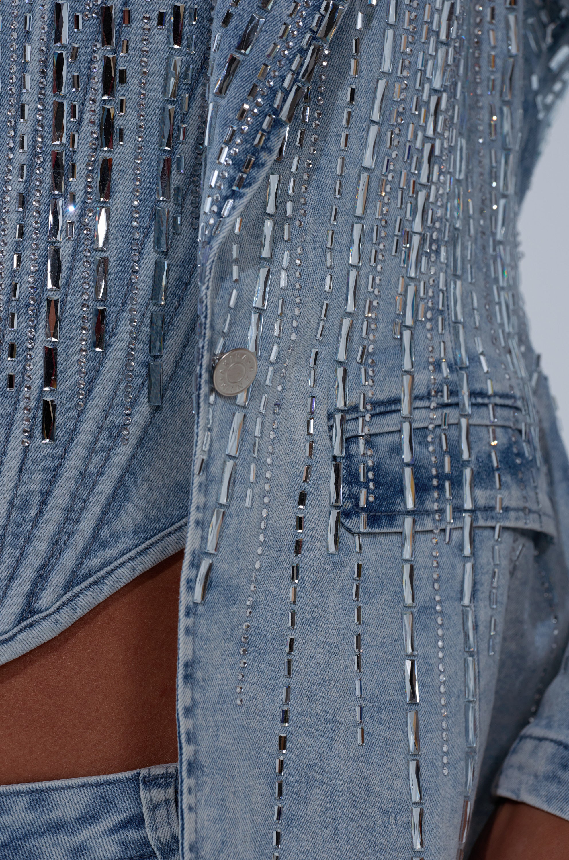 Close-up of the MILA EMBELLISHED BLAZER IN DENIM, featuring vertical rhinestone rows, a button, visible pocket, and a cutout section that reveals skin.
