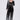 A woman poses in the MILA EMBELLISHED FLARE PANT IN BLACK, featuring vertical silver sequin stripes. She wears a black lace bralette, holds a silver clutch, and stands against a plain light background.