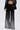 Wearing the MILA EMBELLISHED FLARE PANT IN BLACK with a matching blazer featuring vertical silver rhinestones, a black lace bralette, and holding a small clutch, the person stands against a plain light background.