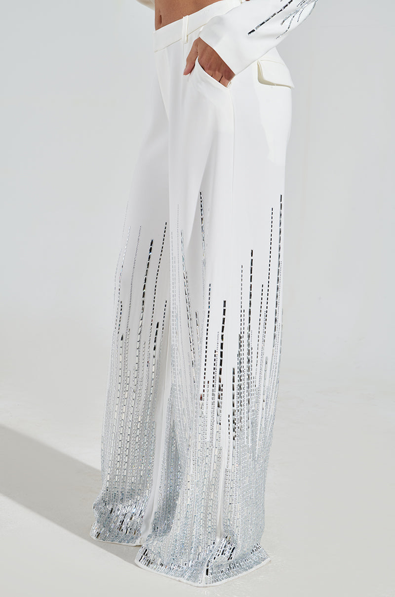 A person wearing the MILA EMBELLISHED FLARE PANT adorned with silver rhinestones in a gradient from hem upwards. These high-rise wide-leg pants feature pockets and are paired with a partially visible white top.