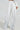Someone is dressed in the MILA EMBELLISHED FLARE PANT, high-rise wide-leg white pants with sparkling silver stripes from waist to hem, featuring two back pockets. They are paired with a matching long-sleeve top.