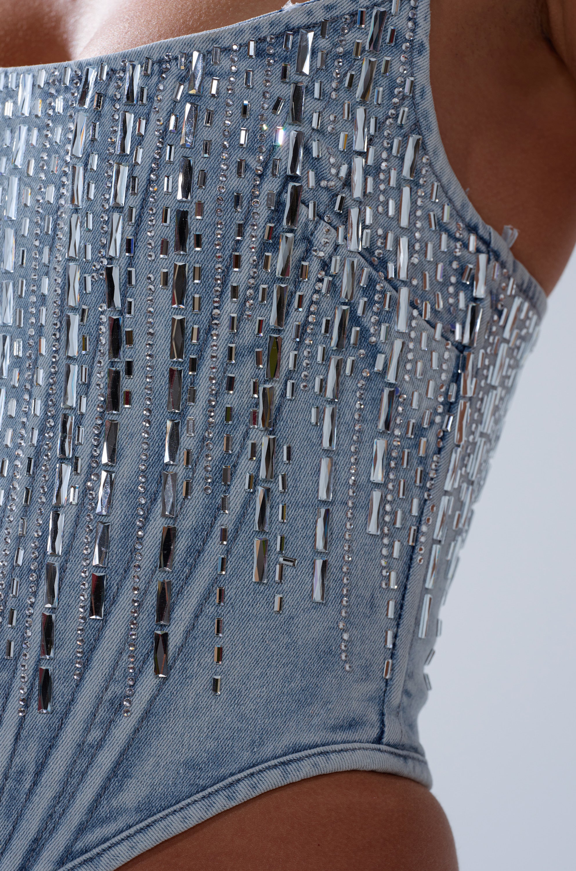 Close-up of a person wearing the MILA EMBELLISHED CORSET IN DENIM, featuring vertical rows of shiny rectangular silver beads that create a sparkling, decorative look.