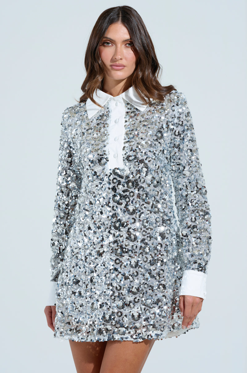 Against a light background, a person showcases the SO POSH BEADED SEQUIN SHIRT DRESS with its long sleeves, front buttons, and exquisite sequin and bead embellishments on a subtle mesh base, complemented by a white collar and cuffs.