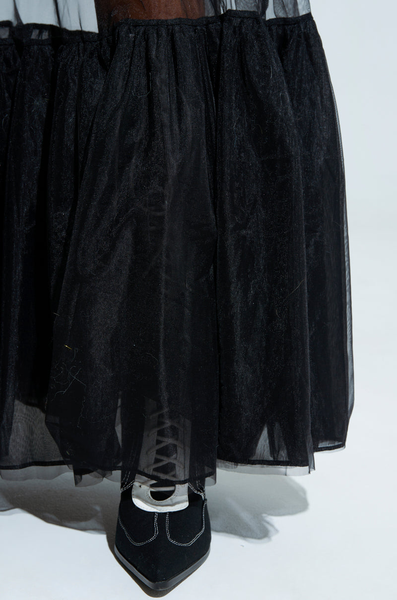 A TRY ME MAXI SKIRT in sheer, black tulle fabric elegantly grazes the floor, revealing a hint of black lace-up shoe beneath its hem and is showcased against a plain white background.