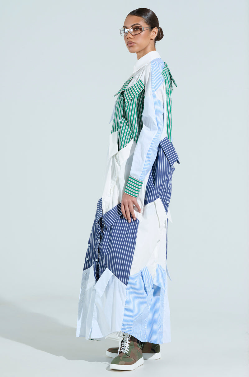 A person wearing glasses models the NOT YOUR BOYFRIEND'S SHIRT MAXI DRESS, showcasing a patchwork design with green, blue, and white stripes. They're paired with brown and green high-top sneakers against a light gray backdrop.