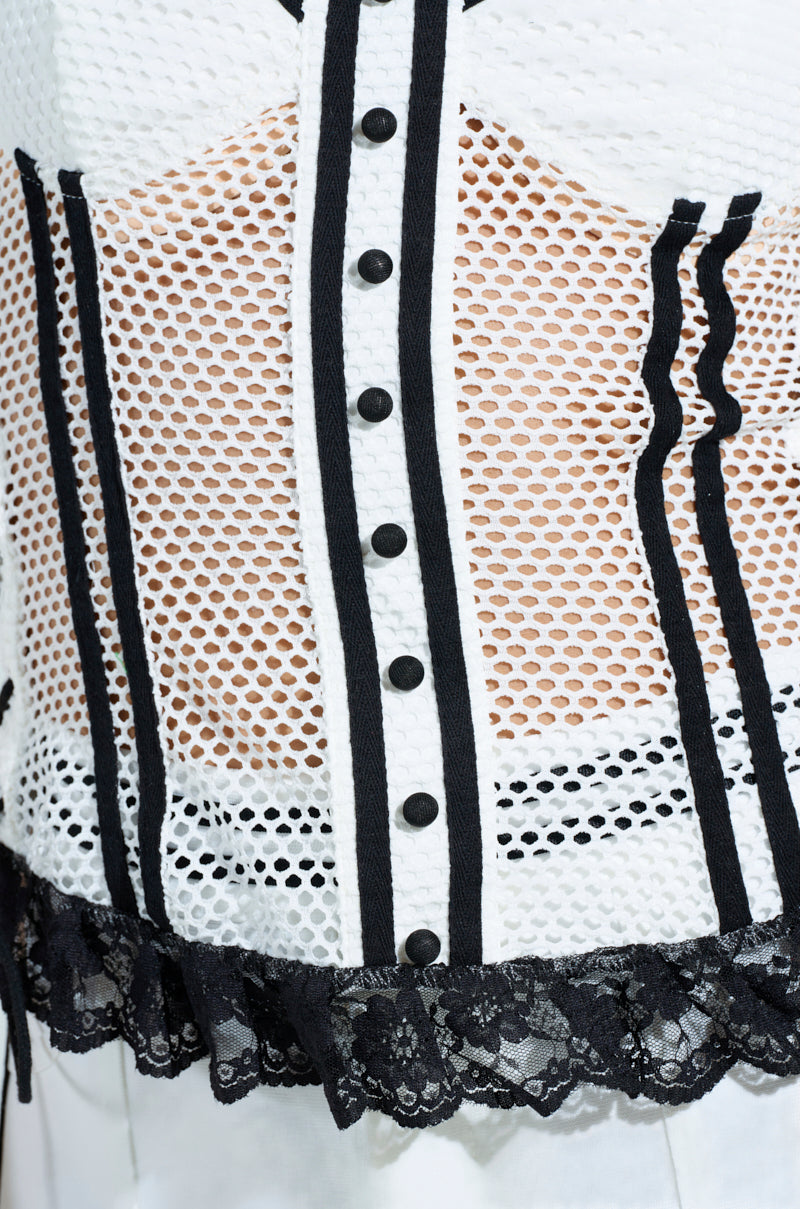 Close-up of the VIVI JERSEY CORSET, a sporty-chic top in white with black vertical lines, buttons, crochet-like perforated jersey mesh, and elegant black lace trim at the bottom edge. 9
