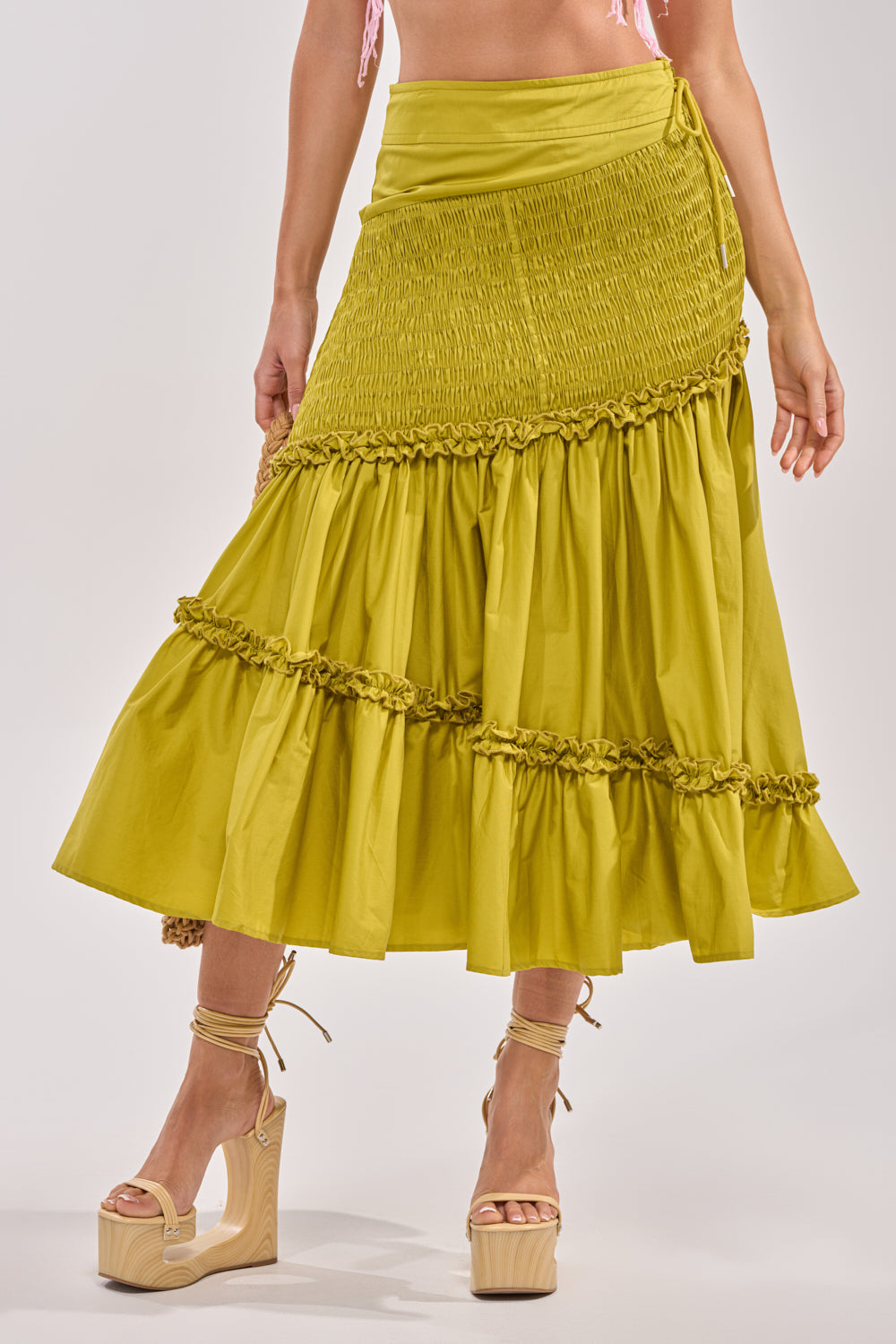 A woman wears the IT ONLY GETS BETTER RUCHED MAXI SKIRT in chartreuse with a smocked waistband, paired with beige platform ankle-strap sandals—ideal for resort style. Only her lower body is shown. 0