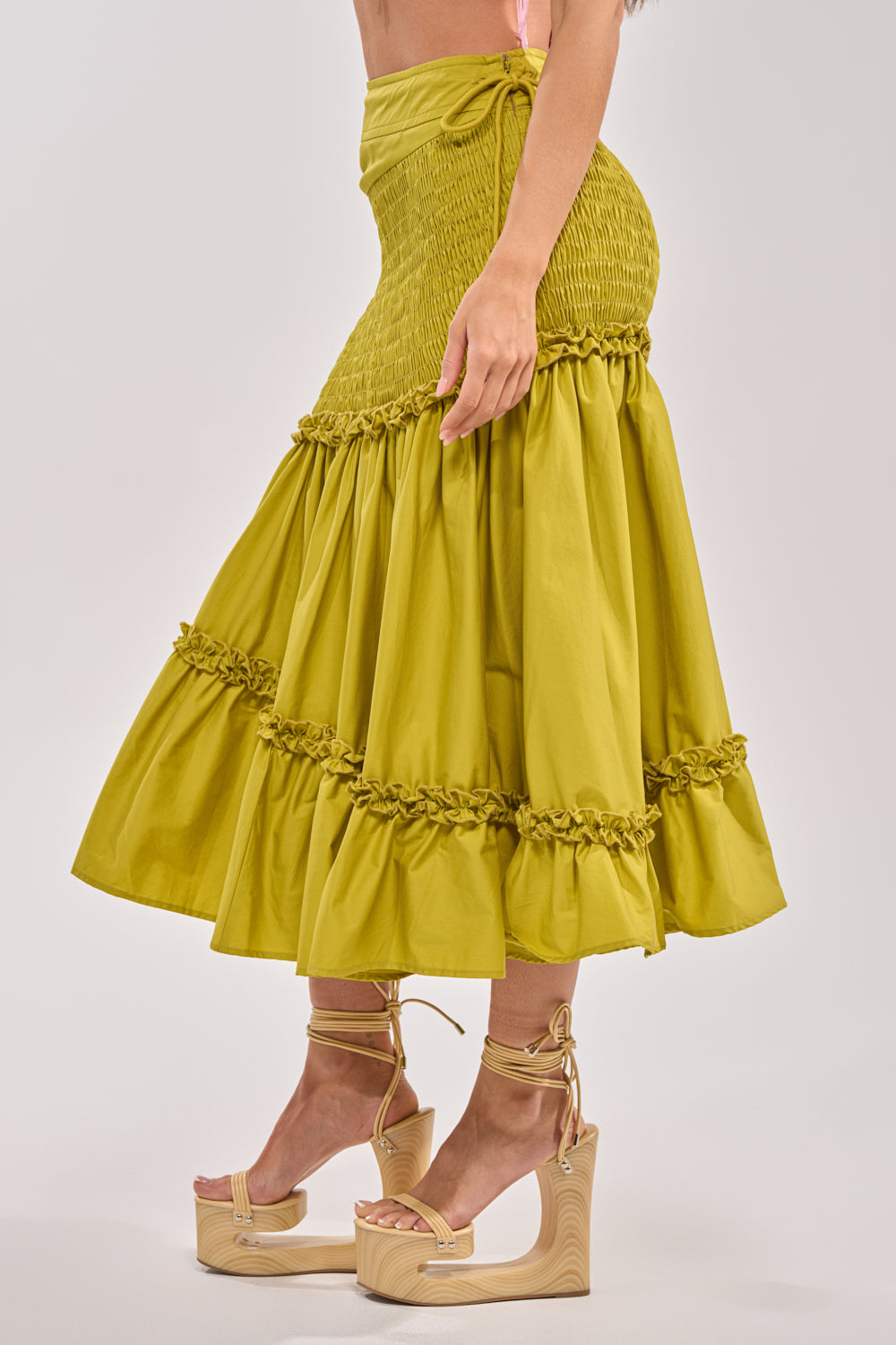 A woman wears the IT ONLY GETS BETTER RUCHED MAXI SKIRT in chartreuse with a smocked waistband and tiered hem, paired with strappy gold platform sandals—ideal for chic resort style. The side photo features a plain background. 2