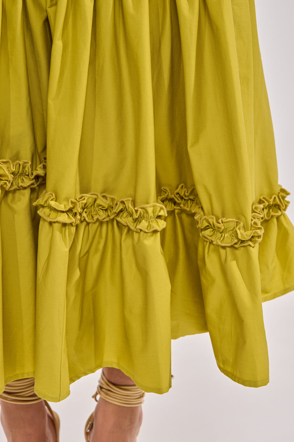A close-up of the IT ONLY GETS BETTER RUCHED MAXI SKIRT in chartreuse, featuring gathered details and visible stitching. The below-the-knee hemline is ideal for resort looks, as the model’s lower legs and strappy sandals are visible. 7