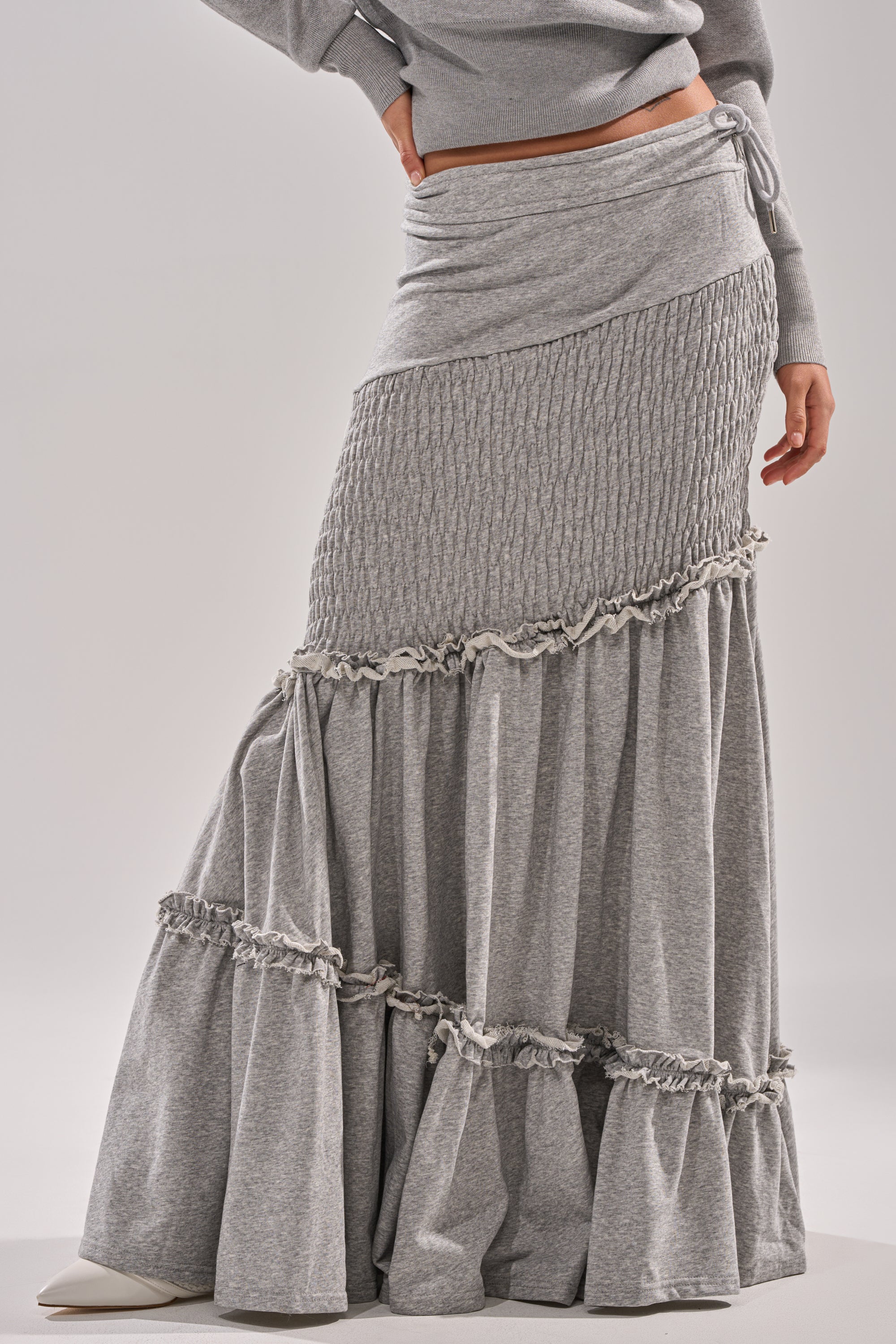 Someone models the IT ONLY GETS BETTER RUCHED MAXI SKIRT IN HEATHER GREY, featuring ruched and ruffled details, paired with a matching top. Only the lower half is visible against a plain background. 1