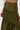 A close-up of a person wearing the IT ONLY GETS BETTER RUCHED MAXI SKIRT in olive green, featuring an asymmetrical high-waist design, paired with a cream long-sleeve top with small gold buttons on the cuffs.